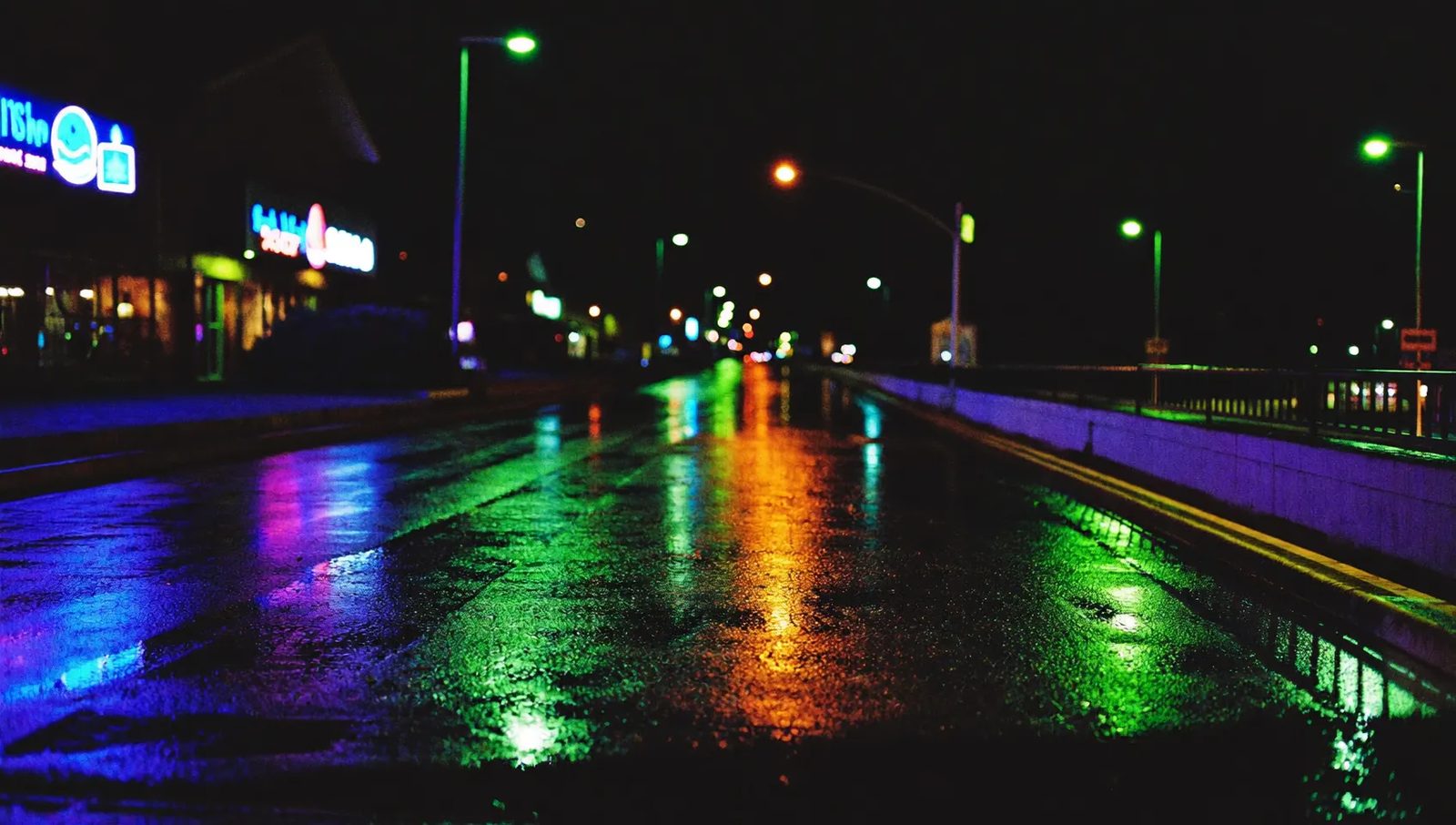 A wet pavement at night with neon colour reflected across it
